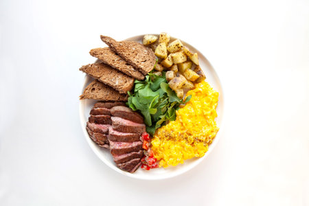 Tenderloin beef steak with scrambled eggs, rocket leaves and potatoes with a side of rye bread.の写真素材