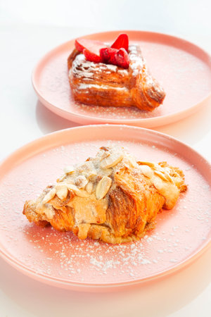 Almond croissant placed on a pink plate with strawberry danish in the background.の写真素材