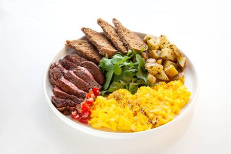 Tenderloin beef steak with scrambled eggs, rocket leaves and potatoes with a side of rye bread.の写真素材