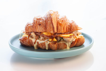 Brioche croissant chicken sandwich on a pink plate white background.の写真素材