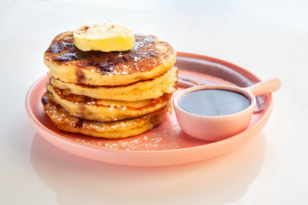 Stack of blue berry pancakes topped with honeycomb butter and maple syrup on a pink plate.の写真素材