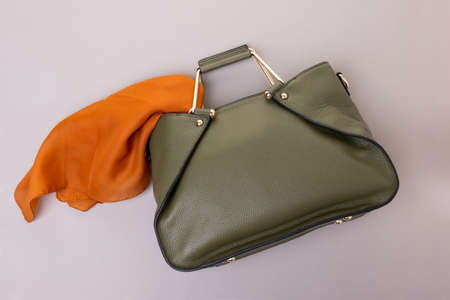Olive-colored leather women's bag with gold metal handles. An orange silk handkerchief in the bag. Gray backgroundの写真素材