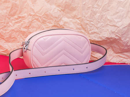 Pink waist bag made of genuine leather. Pink leather belt. Blue and red background, crumpled beige paperの写真素材
