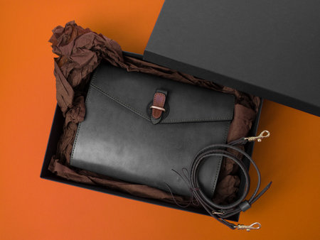 Handmade bag made of genuine gray leather. Packed in a black gift box with brown crumpled paper. Orange backgroundの写真素材