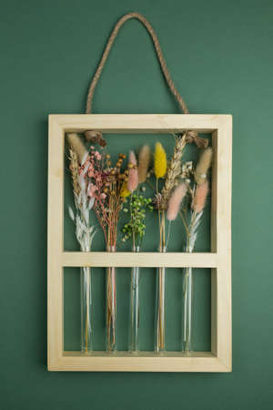 Dried flower arrangement in narrow glass vases in a natural wooden frame with handle. Pink, yellow, beige, white colors. Green backgroundの写真素材