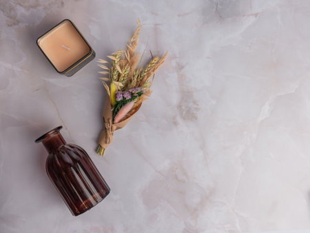 A candle in a box, a brown glass vase, a bouquet of dried flowers on a marble backgroundの写真素材