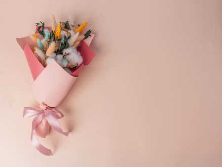 A bouquet of dried flowers in colored paper tied with a pink ribbon. On a pink backgroundの写真素材
