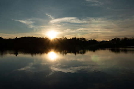 Sunset reflected in the lake as a mirror image. Sunset over the mountains. Clouds in the evening skyの写真素材