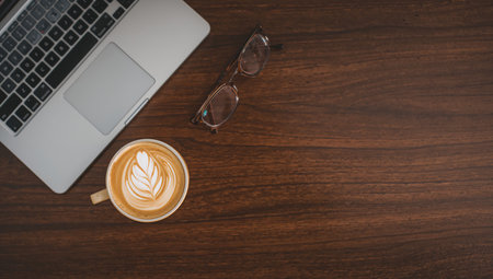 Top view of latte art coffee with laptop and eyeglasses on wooden tableの素材