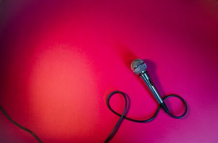 Silver microphone on a red background, with a black cord.の写真素材