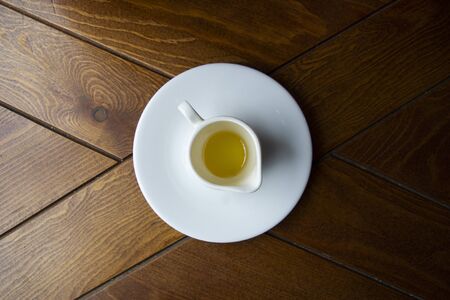 Spring honey with a white cup on a saucer with a green sprig on a wooden table.の写真素材