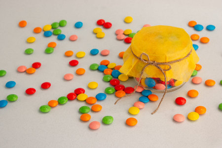 Chocolate candies, small multi-colored in a jar with a bow, on a gray background and with a yellow...