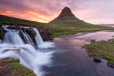 Amazing sunset the top or Kirkjufellsfoss waterfall with Kirkjufell mountain in the background on the north coast of Iceland's Snaefellsnes peninsula duties white a long shutter speed.の写真素材