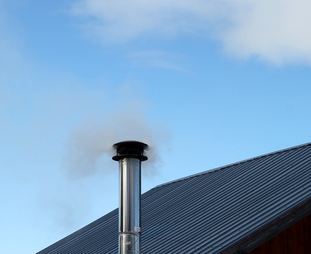 Smoke coming out of a metal chimney on the roof of a residential house with a blue sky in the backgroundの写真素材