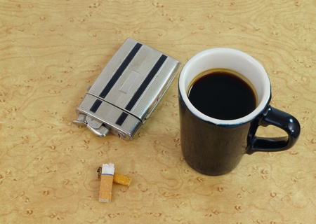 Coffee and cigarettes: Vintage cigarette lighter/case next to a coffee cup on an old tableの写真素材