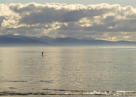 Lone stand up paddle surfer in calm waters of the Kachemak Bay, Alaska at dusk with dramatic storm clouds and mountains in the background.の写真素材
