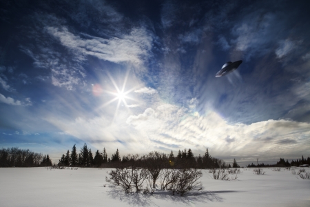 UFO hovering over an Alaskan snow scene with a sunburst and clouds.の写真素材