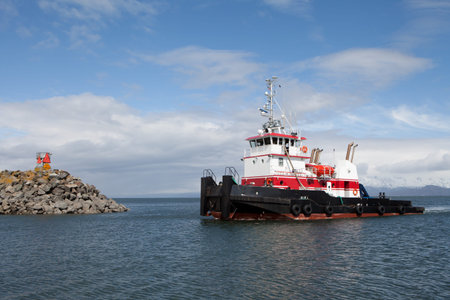 White and red tug boat entering the harbor in Homer, Alaska.