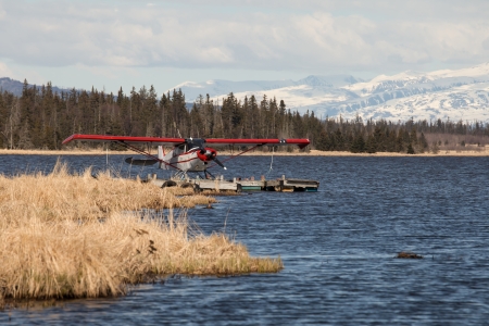 Red floatplane on an Alaskan lake in fall with snow covered mountains and spruce forest in the background.の写真素材