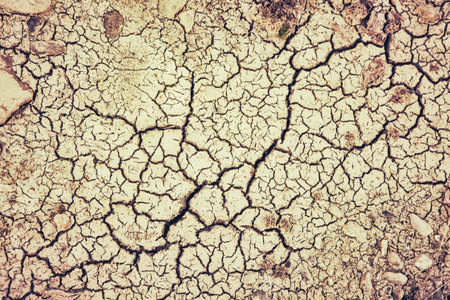 Cracks forming in a dry lake bed during a drought processed with textures for a vintage look.