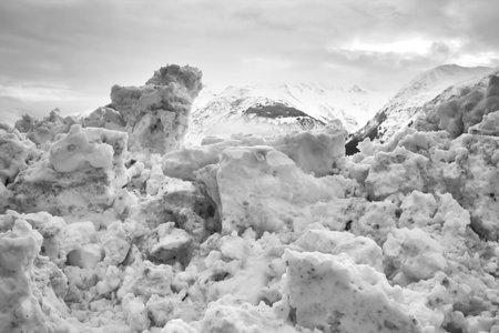 Large pile of old melting snow with mountains in the background in black and white.