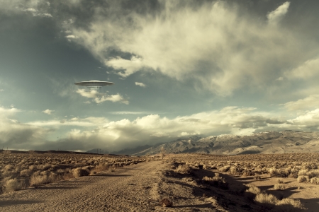 UFO spaceship hovering over a desert road with puffy clouds processed with a vintage look.の写真素材