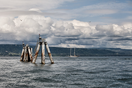 Storm clouds over the Kachemak Bay in Alaska with a sail boat and old pier pillars.の写真素材