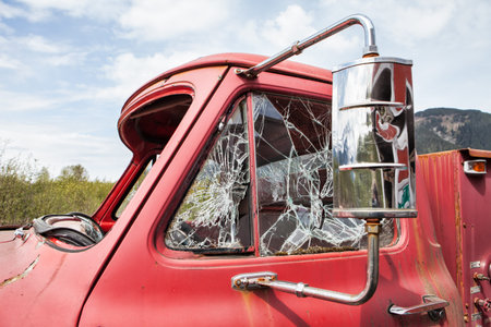 Vintage fire truck with smashed windows against blue sky with clouds.