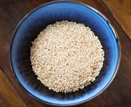 Blue bowl of uncooked brown rice on a wooden table.