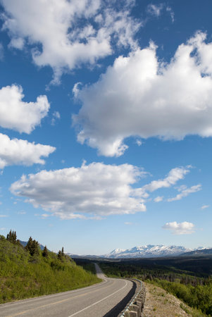 Empty Yukon mountain highway in spring with puffy clouds.