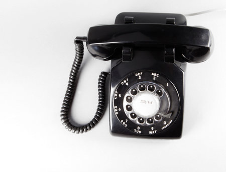 Black vintage rotary telephone on white from above.
