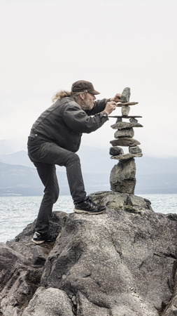 Man carefully stacking rocks in a cairn by the sea.の写真素材