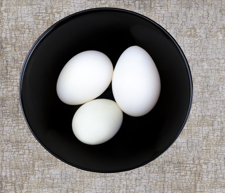 Three large white duck eggs in a black bowl on a textured surface shot from ablove.の写真素材
