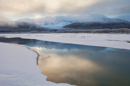 Fog decending on the Chilkat river at sunset with reflections on open water in winter.