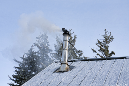 Smoke pouring out of a stove pipe on a metal roof from a wood fire on a winter day.の写真素材