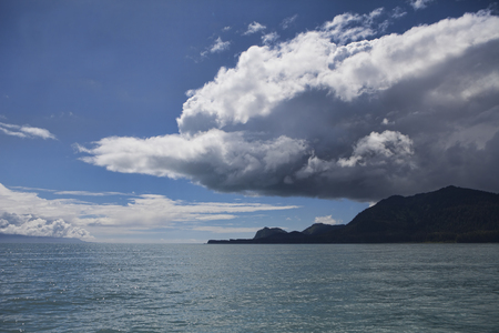 Dark storm cloud forming over an island in Cross Sound in Southeast Alaska in summer as seen from a boat.の写真素材