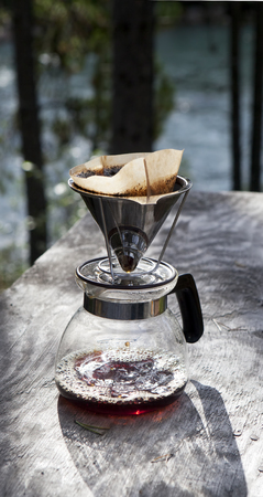 Making coffee with a drip filter holder on a rustic table near a river in summer.の写真素材