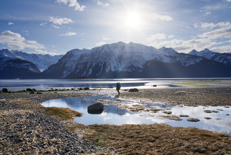 Man with a tripod walking on a beautiful beach near Haines Alaska as the tide goes out with mountains in the background.の写真素材