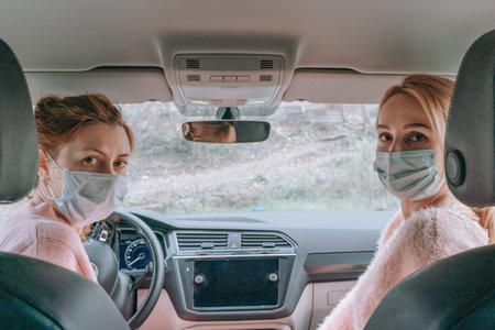 two Masked European girls sit in the front seats of the car and turn back