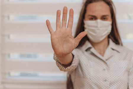 Close-up portrait of a young blonde woman in a medical mask on a light background. Virus protection....
