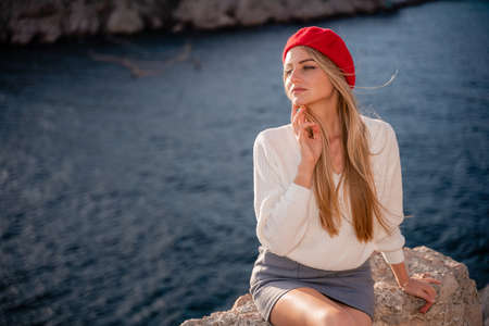 Beautiful blonde with long straight hair in a white sweater and red beret on the background of the sea. Portrait of a girl.の写真素材