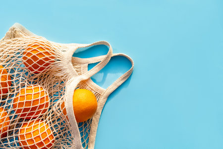 Mesh white cotton reusable bag with oranges on a blue background. Environmentally friendly shopping, the environment and the concept of healthy foods, citrus fruits with vitamin C. Place for textの写真素材