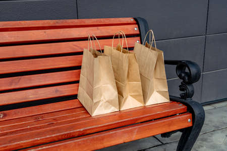 Three craft paper bags on a wooden bench near the store.の写真素材