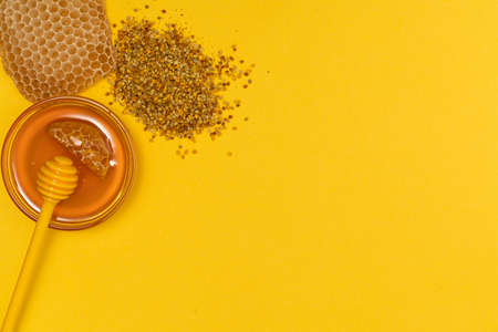 A ladle of honey on the background of a honeycomb of a bee. Honey tidbit in a glass jar honey spoon, bee bread and a honeycomb of wax on a yellow background. Healthy food concept.の写真素材