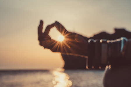 In blur closeup the hand of a young woman in bracelets. Practicing yoga on the beach with sunset. Keeps fingers connected, the sun shines through them. The concept of a healthy lifestyle, harmony.の写真素材