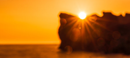 Banner. In blur An epic sunset on the sea - the sun sets behind the mountain and everything shines with warm light with long rays.の写真素材
