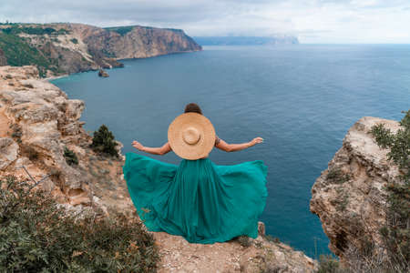 A beautiful girl in a green dress runs to the sea, against the background of large rocks and the seaの写真素材