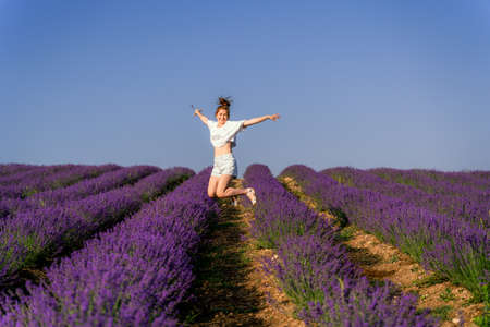 Redhead white woman in white shirt on lavender field smiling, looking at camera and jumpingの写真素材