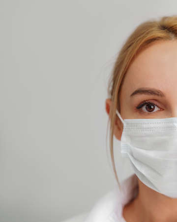 Close-up portrait of a young blonde woman in a medical mask on a light background. Virus protection.の写真素材