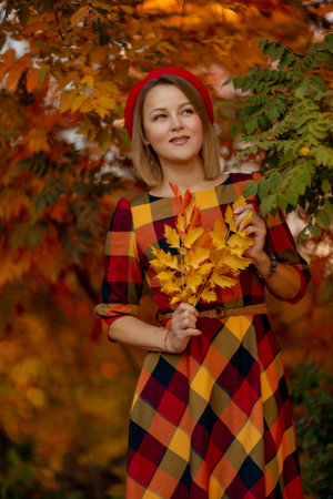Beautiful girl walking outdoors in autumn. Smiling girl collects yellow leaves in autumn. Young woman enjoying autumn weather.の写真素材